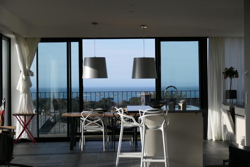 - une salle à manger avec une table, des chaises et de grandes fenêtres dans l'établissement Villa Dremmwel - Villa d'architecte vue mer panoramique, à Penvénan