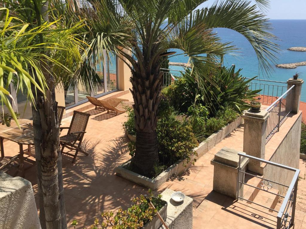 a patio with chairs and palm trees and the ocean at Villa l'ensoleillée vue panoramique mer, 250 m de la plage et du centre ville in Menton