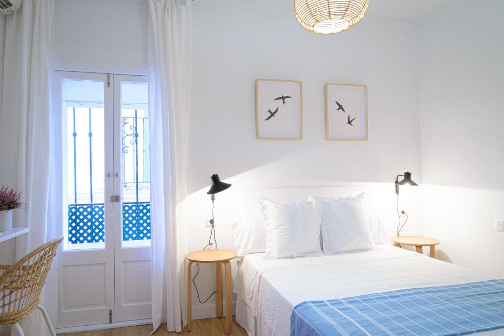 a white bedroom with a bed with a blue blanket at Hostal La Calzada in Tarifa