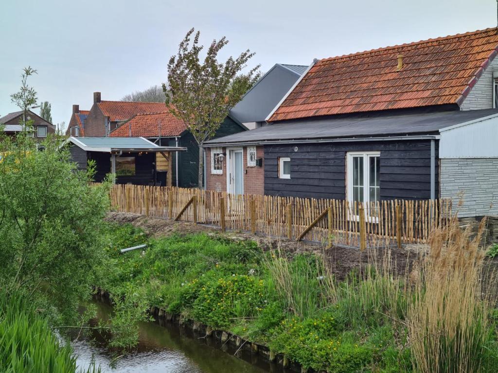 una casa con una valla de madera junto a un río en Schwone Diekhuusje - Vakantiewoning aan de Noordzeekust, en Schoondijke
