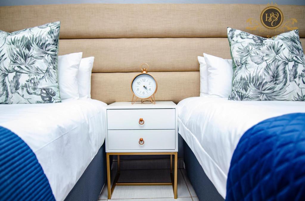 2 Einzelbetten mit einer Uhr auf einem Nachttisch zwischen ihnen in der Unterkunft House of Sollys Guesthouse in Manamane