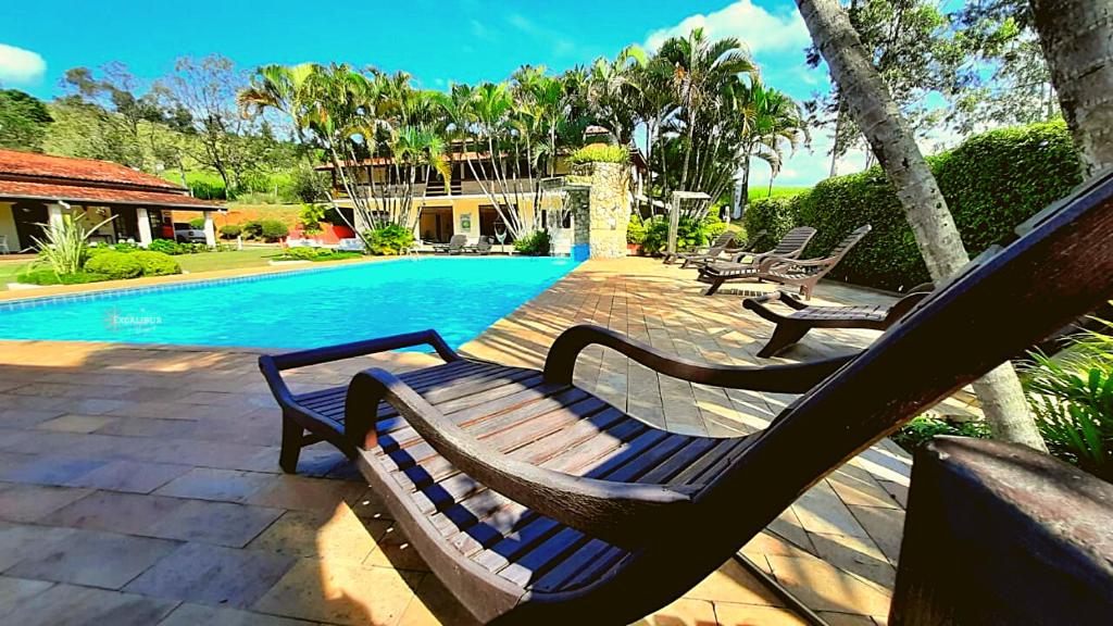 um par de bancos sentados ao lado de uma piscina em Pousada Recanto Por do Sol em Morungaba
