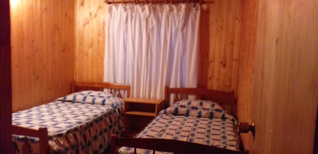 two twin beds in a room with wooden walls at Hospedaje Picoyo in Pucón