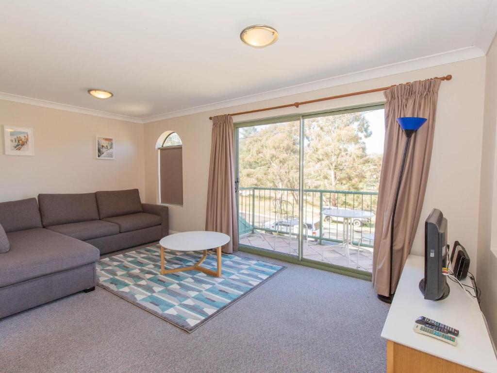 ein Wohnzimmer mit einem Sofa, einem TV und einem Balkon in der Unterkunft Cobb and Co 3 39 Cobbon Cres in Jindabyne
