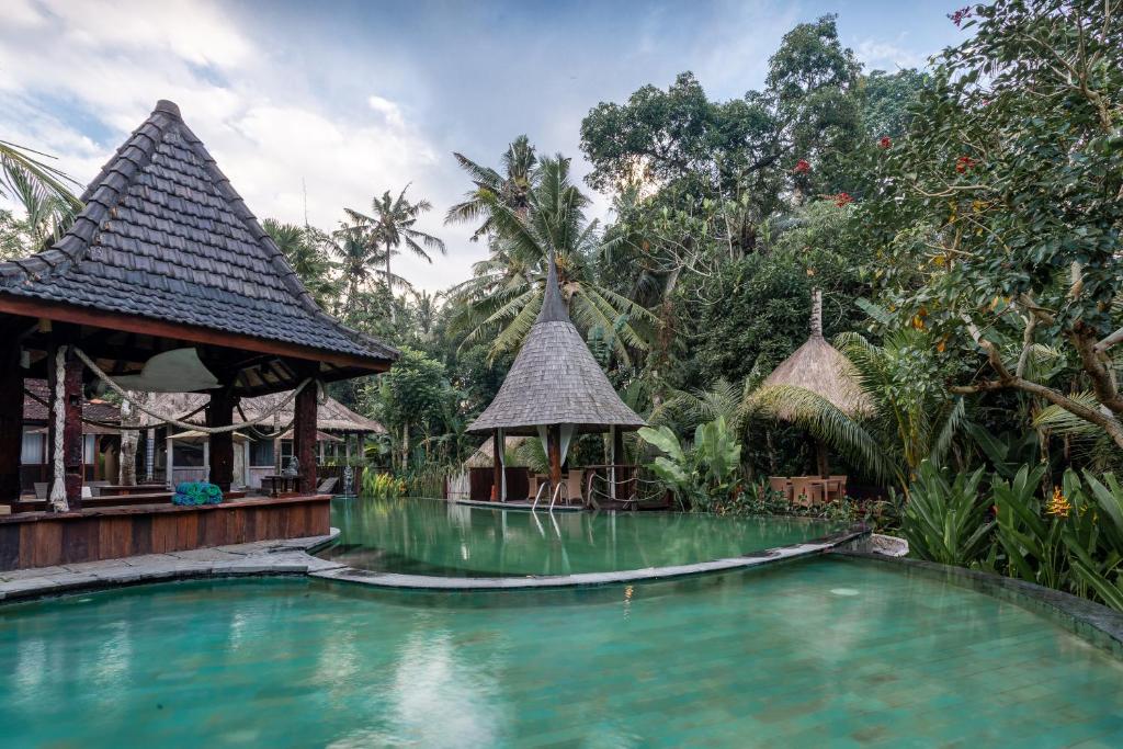 a swimming pool in front of a resort with trees at Keramas Sacred River Retreat Resort and Villa in Keramas