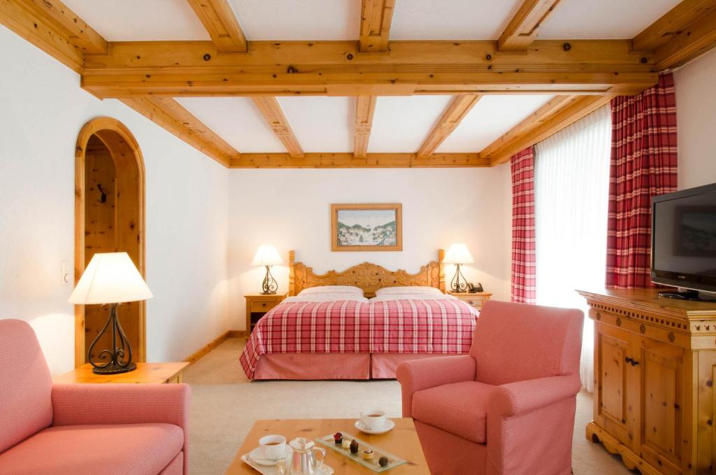 a bedroom with a bed and two chairs and a tv at Crystal Hotel superior in St. Moritz