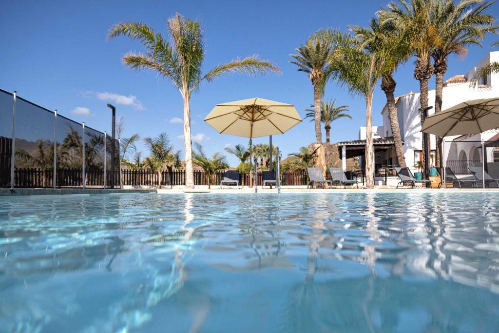 a swimming pool with umbrellas and palm trees at Jardines de la Mata Boutique Beach in Mojácar