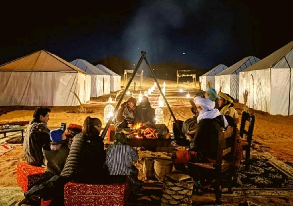 een groep mensen die 's nachts rond een kampvuur zitten bij Morocco Luxury Camp - Merzouga Desert Retreat in Merzouga