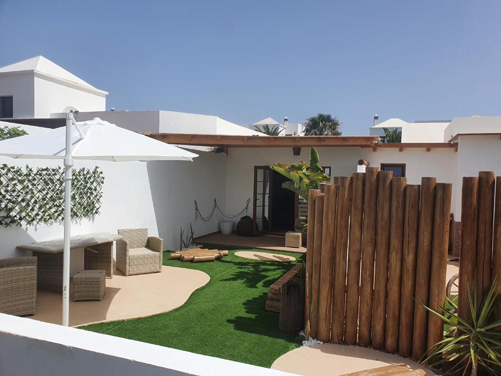 a backyard with a fence and an umbrella and grass at Green Corner Apartment in Yaiza
