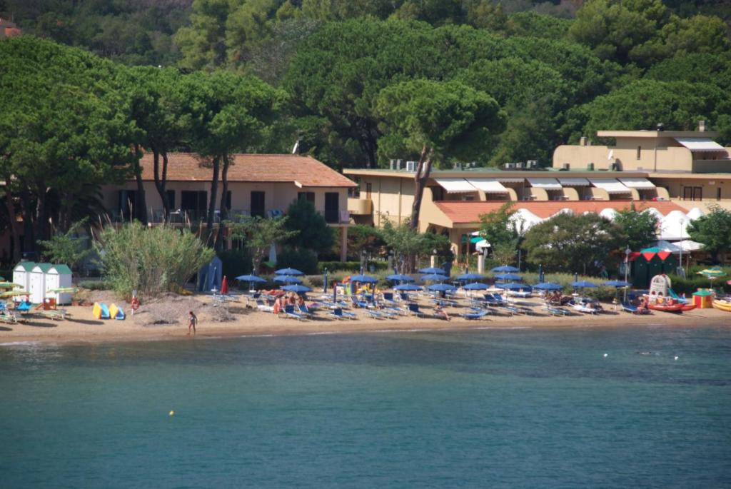 a beach with chairs and umbrellas and a resort at Hotel Voce del Mare in Capoliveri