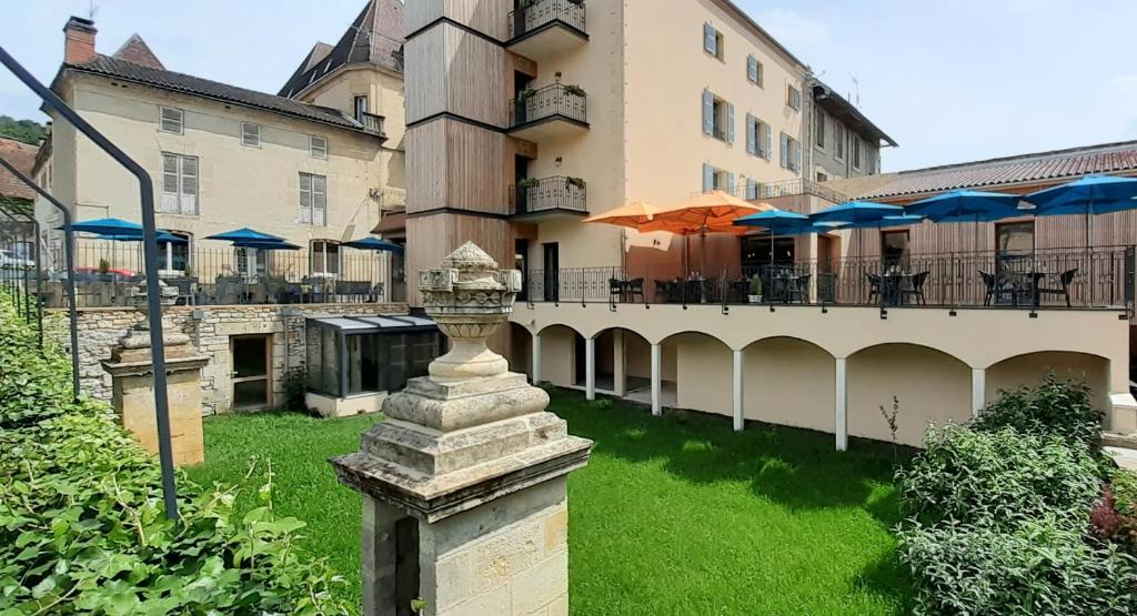 a building with a courtyard with tables and umbrellas at Hotel-Restaurant des Augustins - Cosy Places by CC - Proche Sarlat in Saint-Cyprien