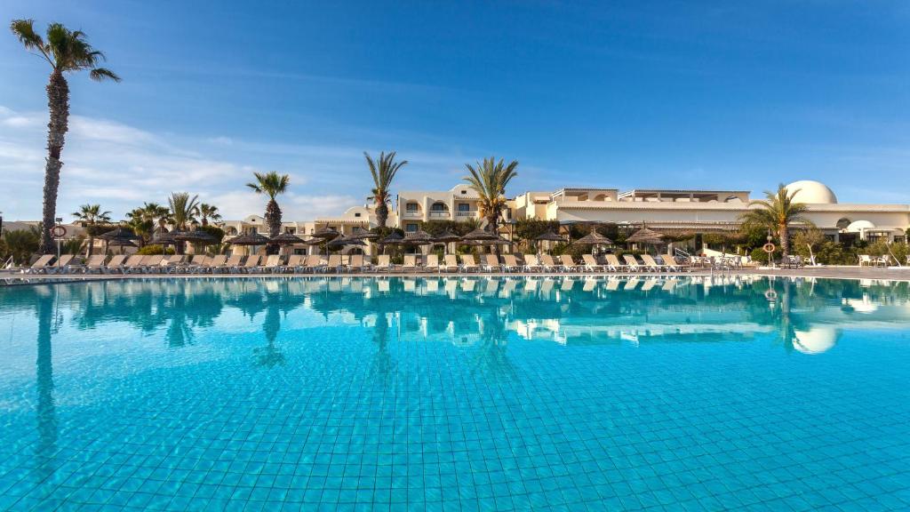 a large blue swimming pool with chairs and palm trees at Djerba Aqua Resort in Midoun