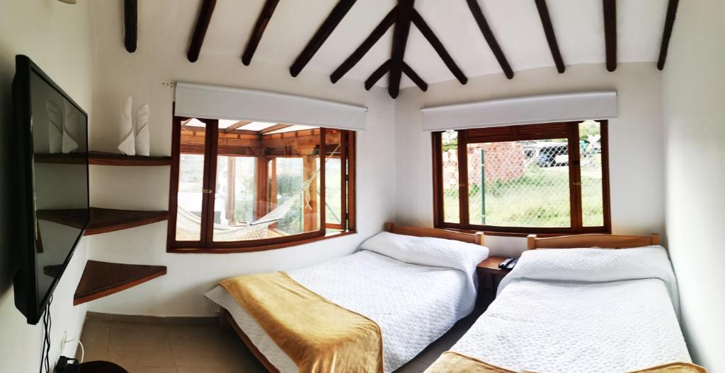 a bedroom with two beds and two windows at Villa Monica HR in Villa de Leyva