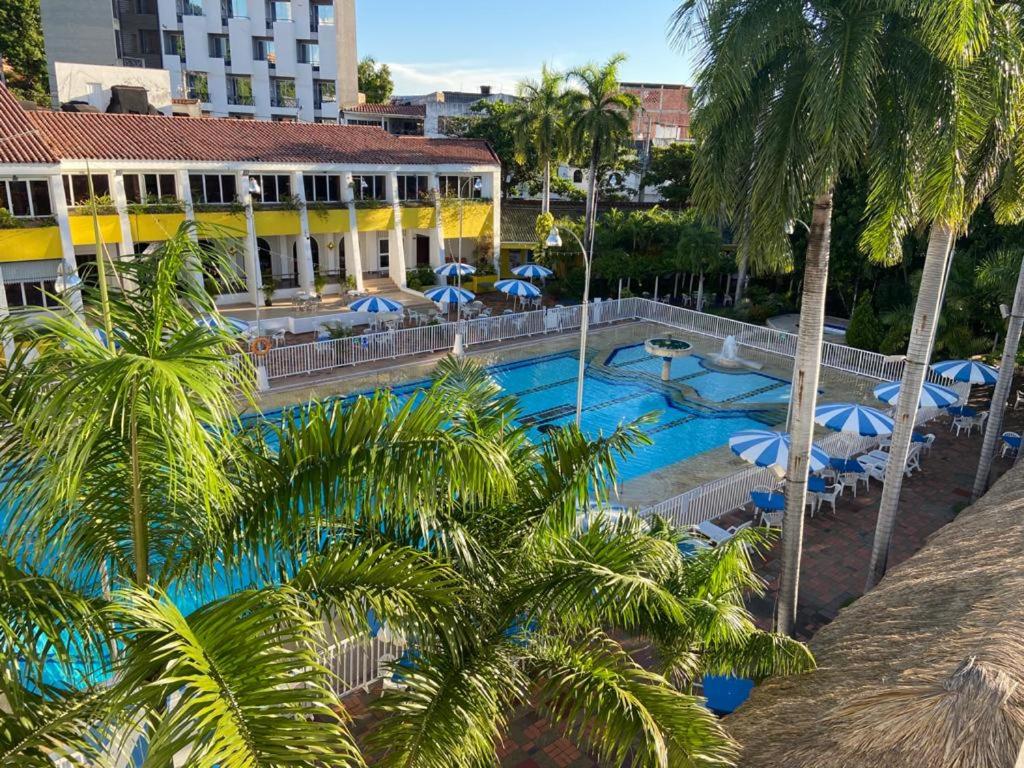 a pool with palm trees and umbrellas and a hotel at Hotel Bachue Girardot in Girardot