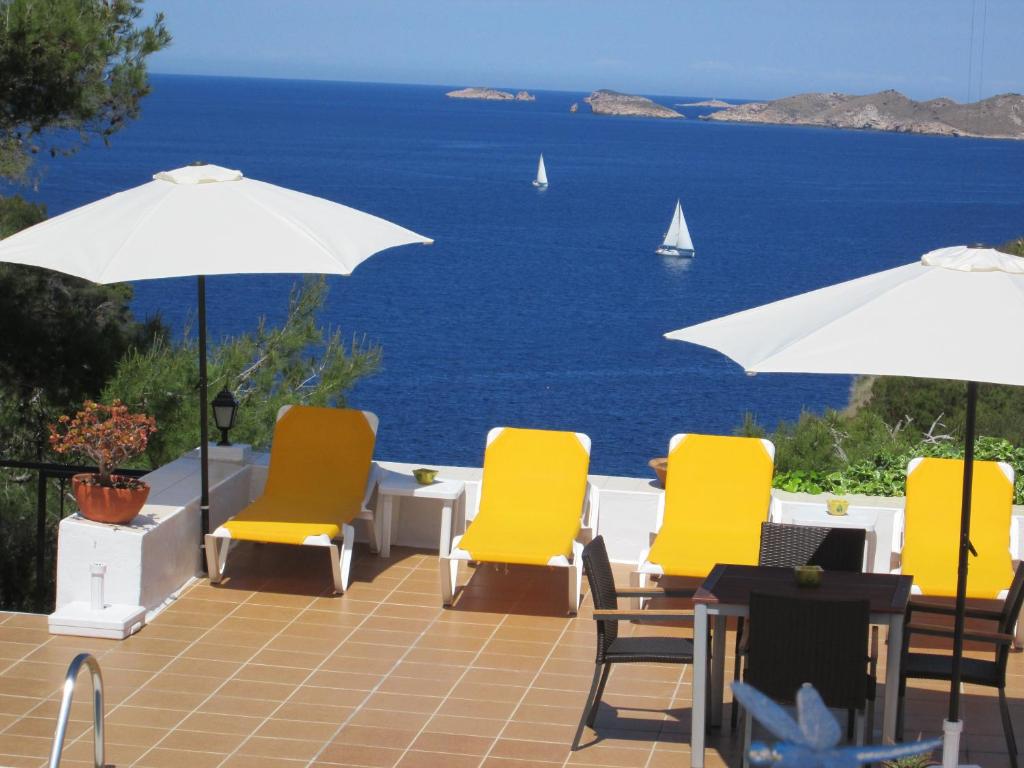 een patio met stoelen en parasols en uitzicht op de oceaan bij Hostal Cala Moli in Cala Tarida