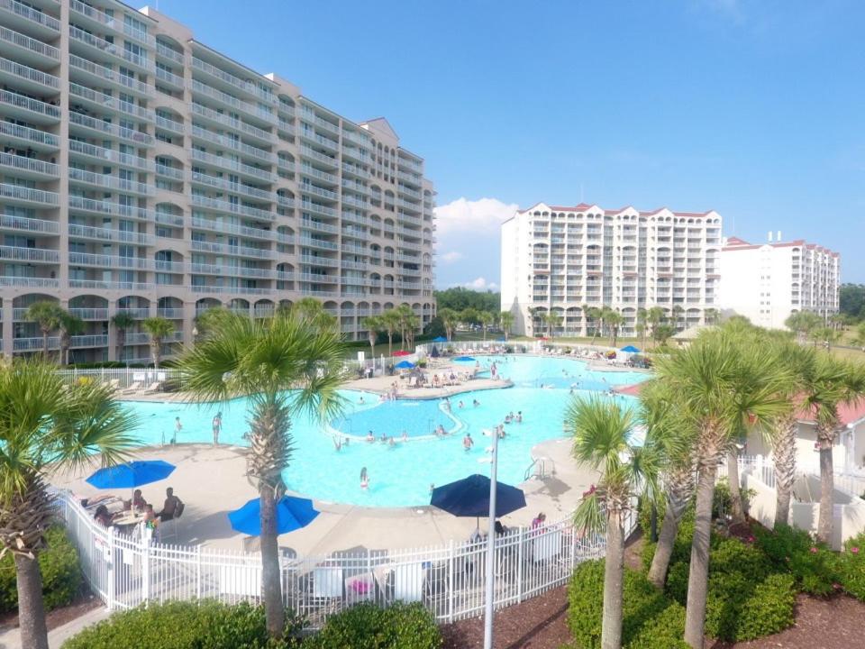 a large swimming pool with palm trees and buildings at Yacht Club Villas #1-202 condo in Myrtle Beach