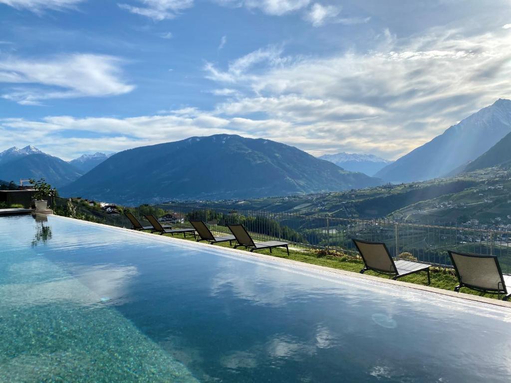 einen Pool mit Stühlen und Bergen im Hintergrund in der Unterkunft Lifestyle Hotel Alpin in Schenna