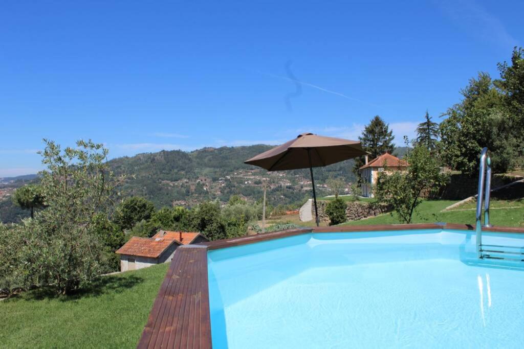 uma piscina com um guarda-sol e uma casa em Casa de Campo - Cinfães do Douro em Cinfães