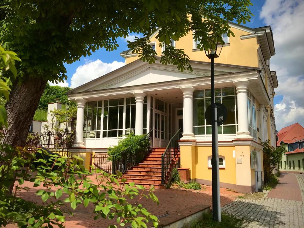 une maison jaune avec une terrasse couverte et des escaliers dans l'établissement Bellevue Gastgeberei, à Buckow