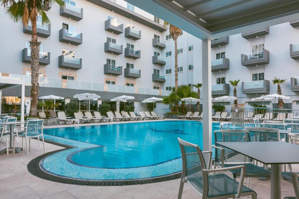 einen Pool mit Stühlen und Tischen vor einem Hotel in der Unterkunft Bora Bora Ibiza Malta Resort - Music Hotel - Adults Only 18 plus in St Paul's Bay