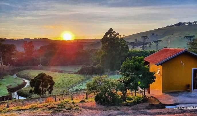 una pintura de una casa con la puesta de sol en el fondo en Pousada e Camping Pé na Trilha, en Bueno Brandão