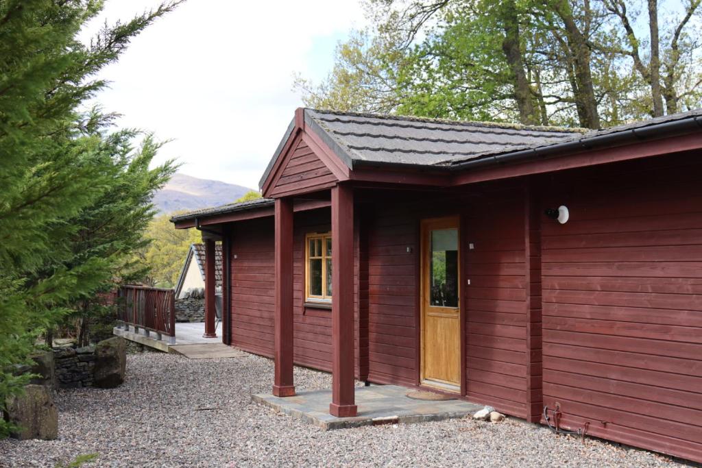 uma cabina vermelha com um alpendre e uma porta em Lodge 37 Rowardennan, Loch Lomond em Glasgow