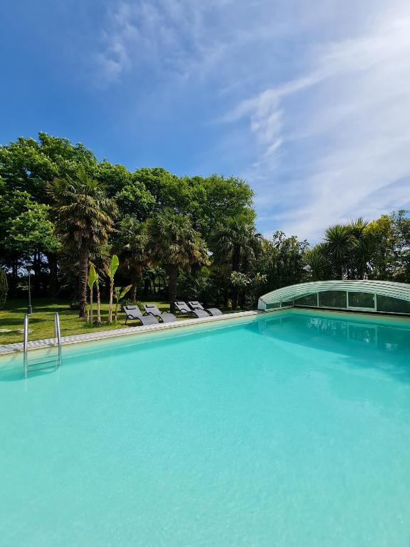 a large blue swimming pool with chairs and trees at Gîte "Tahiti", piscine chauffée in La Roche-sur-Yon