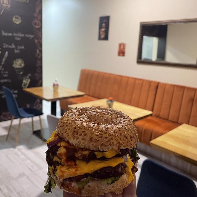 a person holding a bagel sandwich in a restaurant at Wanted Šabac apartman in Šabac