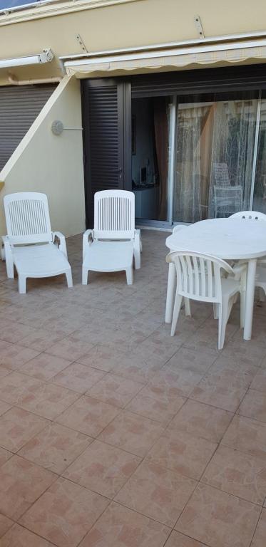 tres bancos blancos y una mesa en un patio en Studio Naturiste "Relax" Héliopolis E 88, en Cap d'Agde