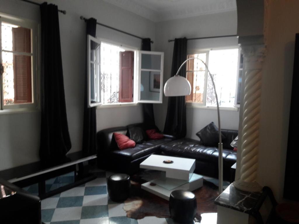 a living room with a black couch and two windows at Appartement Maroc Safi in Safi
