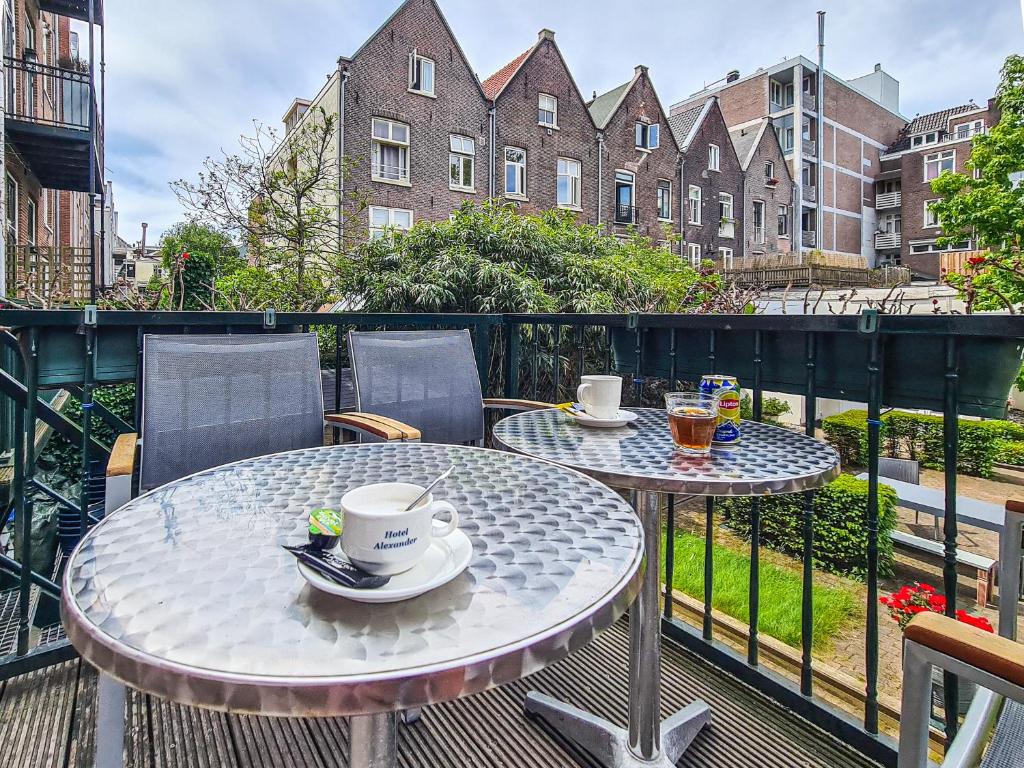 deux tables avec des tasses et des soucoupes sur un balcon dans l'établissement Hotel Alexander, à Amsterdam