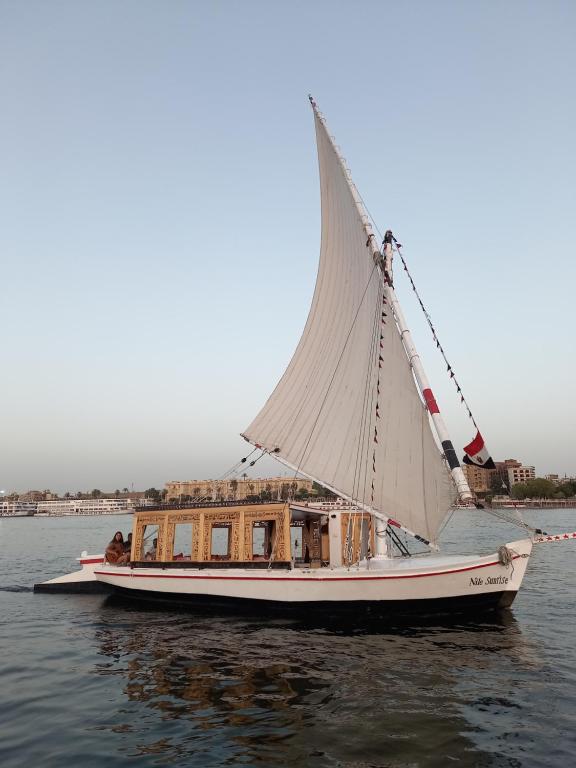 ein Boot mit einem großen weißen Segel auf dem Wasser in der Unterkunft Nile Sunrise Felucca Boat Private Rental in Luxor