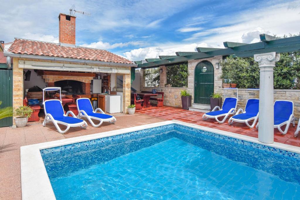 a swimming pool with blue chairs and a house at Apartments Jacqueline in Pakoštane