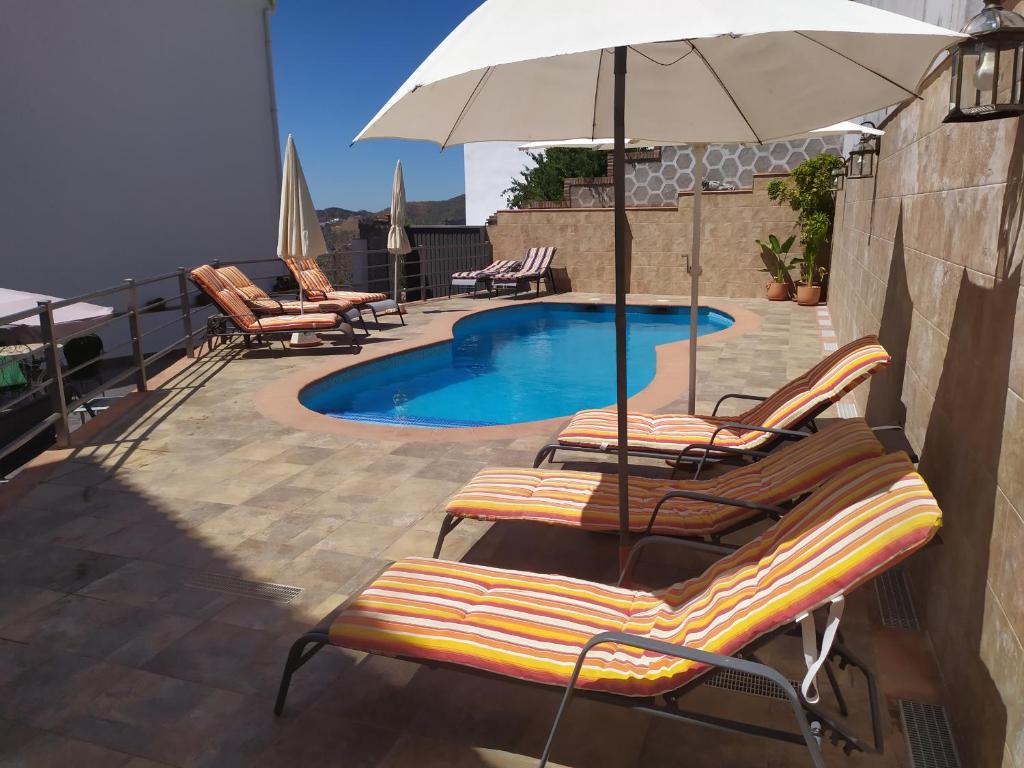 eine Gruppe Stühle und ein Sonnenschirm neben einem Pool in der Unterkunft Apartamentos Maria in Cómpeta