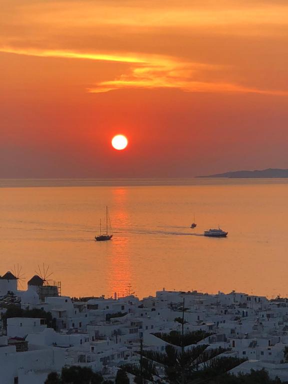 a sunset over the ocean with boats in the water at Ibiscus Boutique in Mikonos