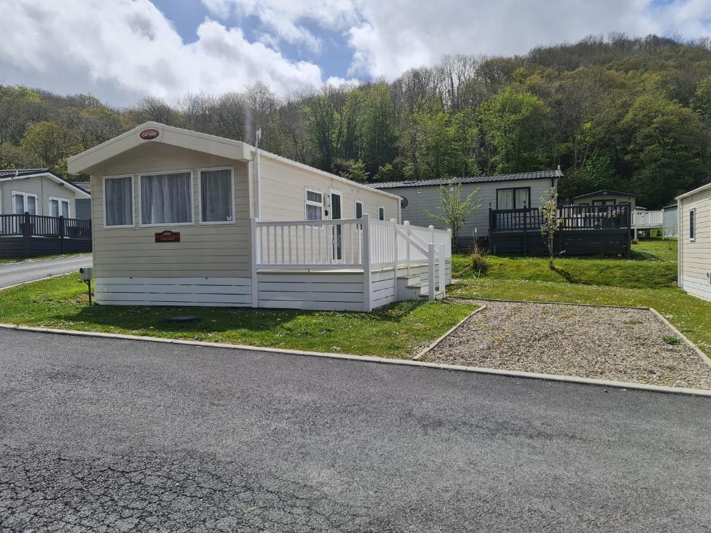 a white house with a porch on the side of a road at The Tiddler - Plot 101, Woodlands Lodge Retreat, New Quay, West Wales in Llanina