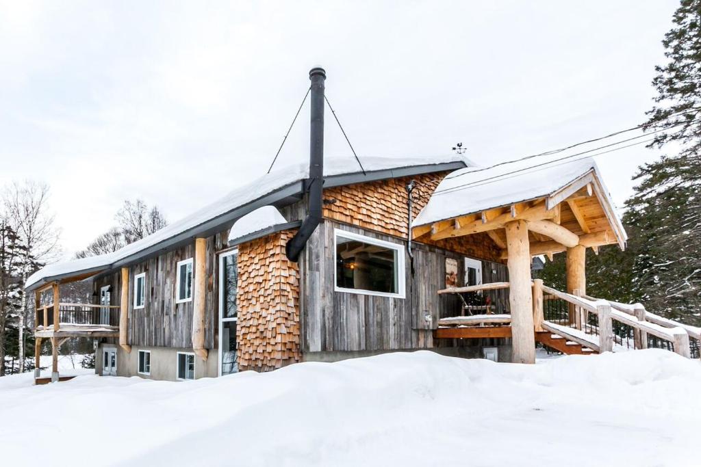een blokhut in de sneeuw met een veranda bij Le Grand Lodge - Locations du Sommet in Saint Adolphe D'Howard