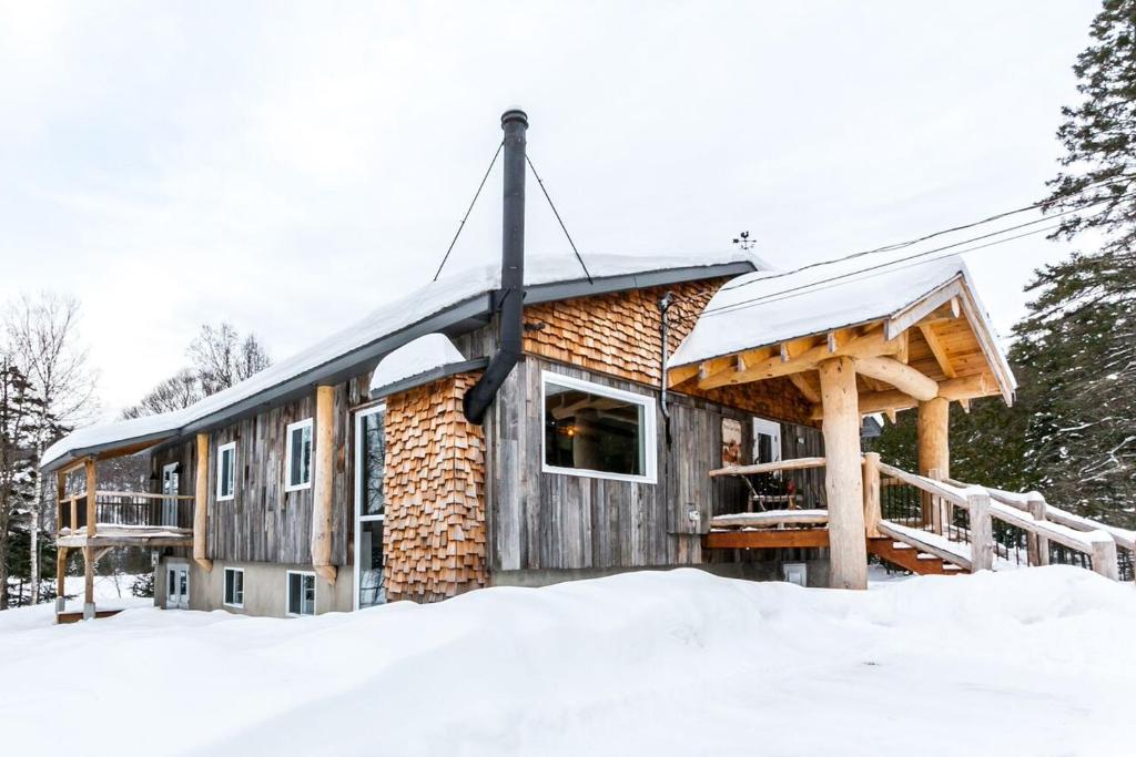 a log cabin in the snow with a porch at Le Grand Lodge - Locations du Sommet in Saint Adolphe D'Howard