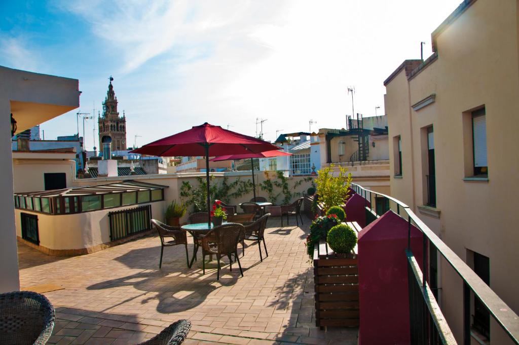 eine Terrasse mit Tischen, Stühlen und einem Sonnenschirm auf dem Balkon in der Unterkunft Hostal Callejon del Agua in Sevilla