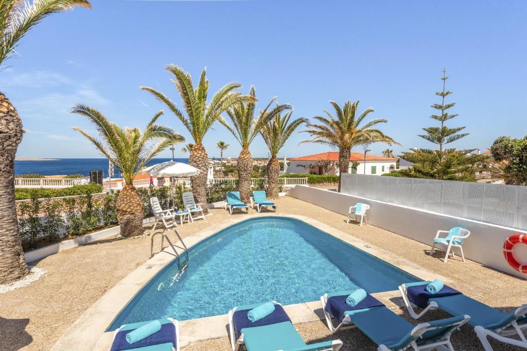 una piscina con sedie, palme e l'oceano di Villa Lali ad Arenal d'en Castell