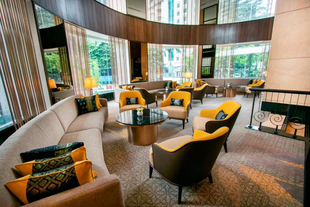 A high-ceilinged lobby lounge with curved seating, mustard armchairs and tall windows.