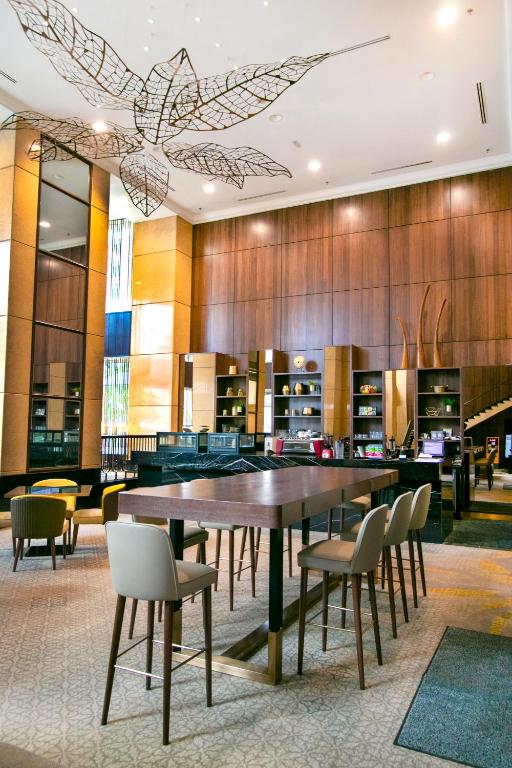 A high-ceilinged lounge or dining area with a communal table and decorative leaf installation.