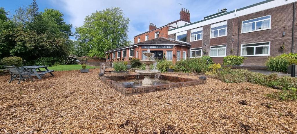 a garden with a fountain in front of a building at Birch Hotel in Heywood