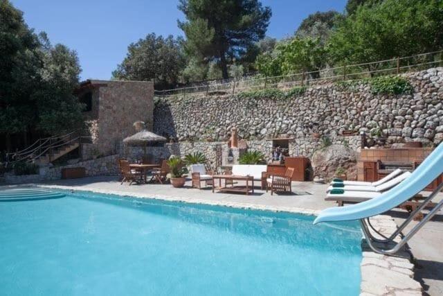 una piscina con sedie e tavoli e un muro in pietra di Fabulous Rustic Villa Set On Mountain With Unique Views a Valldemossa