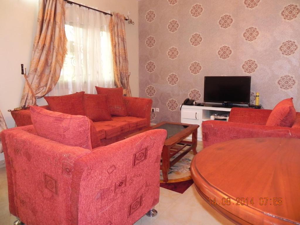 a living room with red chairs and a table and a tv at Résidence La ROSÉE in Yaoundé