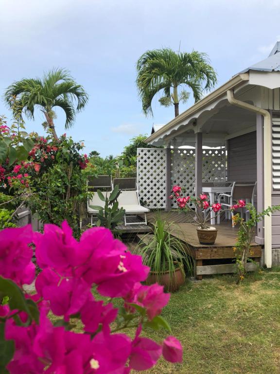 a house with a deck with pink flowers and palm trees at TI-MANGO VUE MER in Sainte-Anne