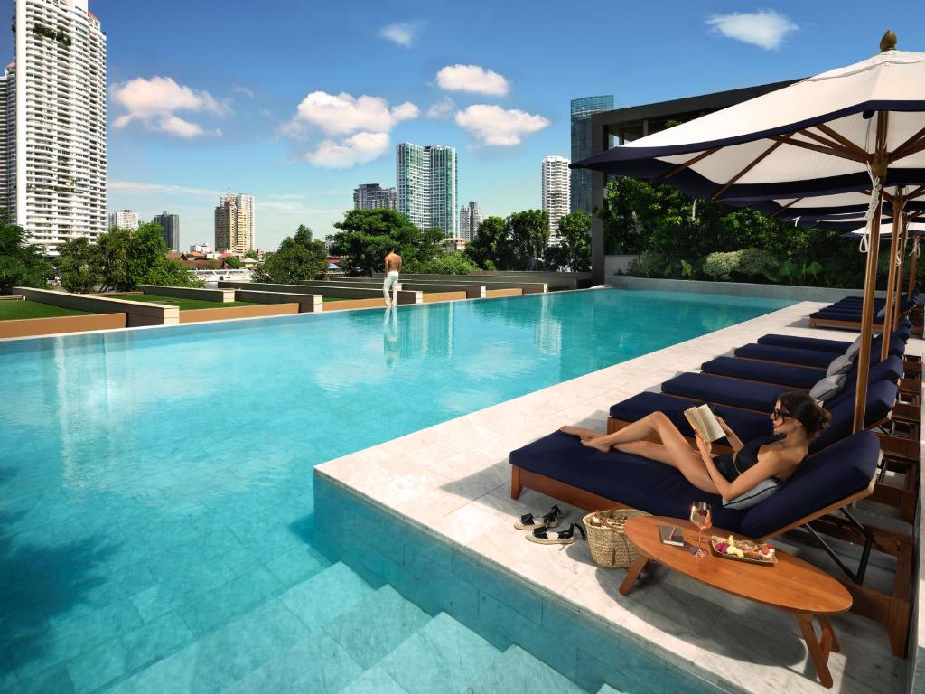 A rooftop-style pool terrace with loungers, umbrellas, and a city skyline.