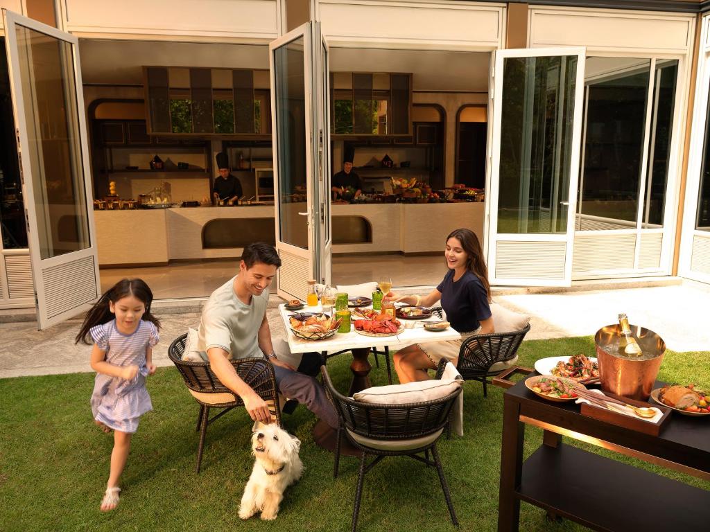 A family shares an outdoor meal beside an open dining room, with a small dog nearby.