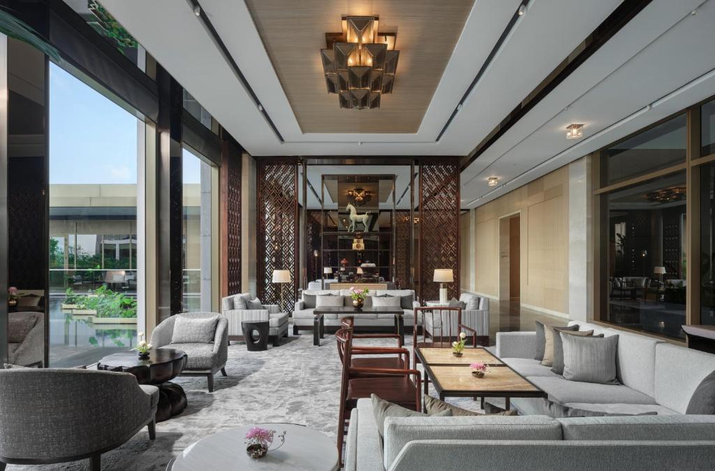 A quiet hotel lounge with layered seating, tall windows, and a view toward greenery.