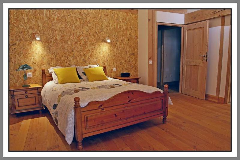 LES CHAMBRES DE LIANE في Cerdon: غرفة نوم بسرير خشبي مع وسادتين صفراء